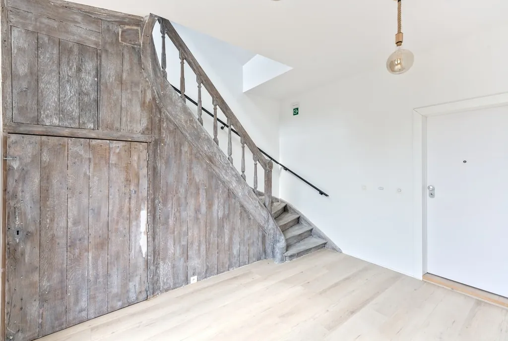 Escalier en bois ancien conservé dans un intérieur rénové aux murs blancs