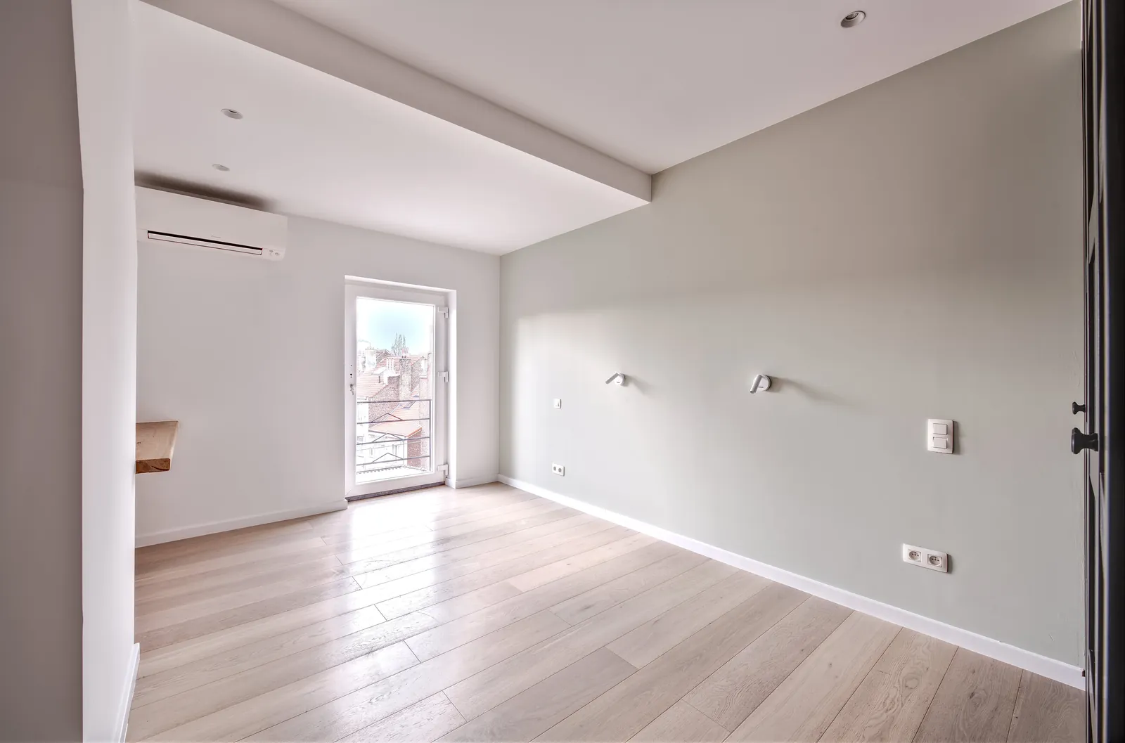 Séjour d'appartement rénové, parquet clair et murs blancs, fenêtre en fond donnant sur les toits